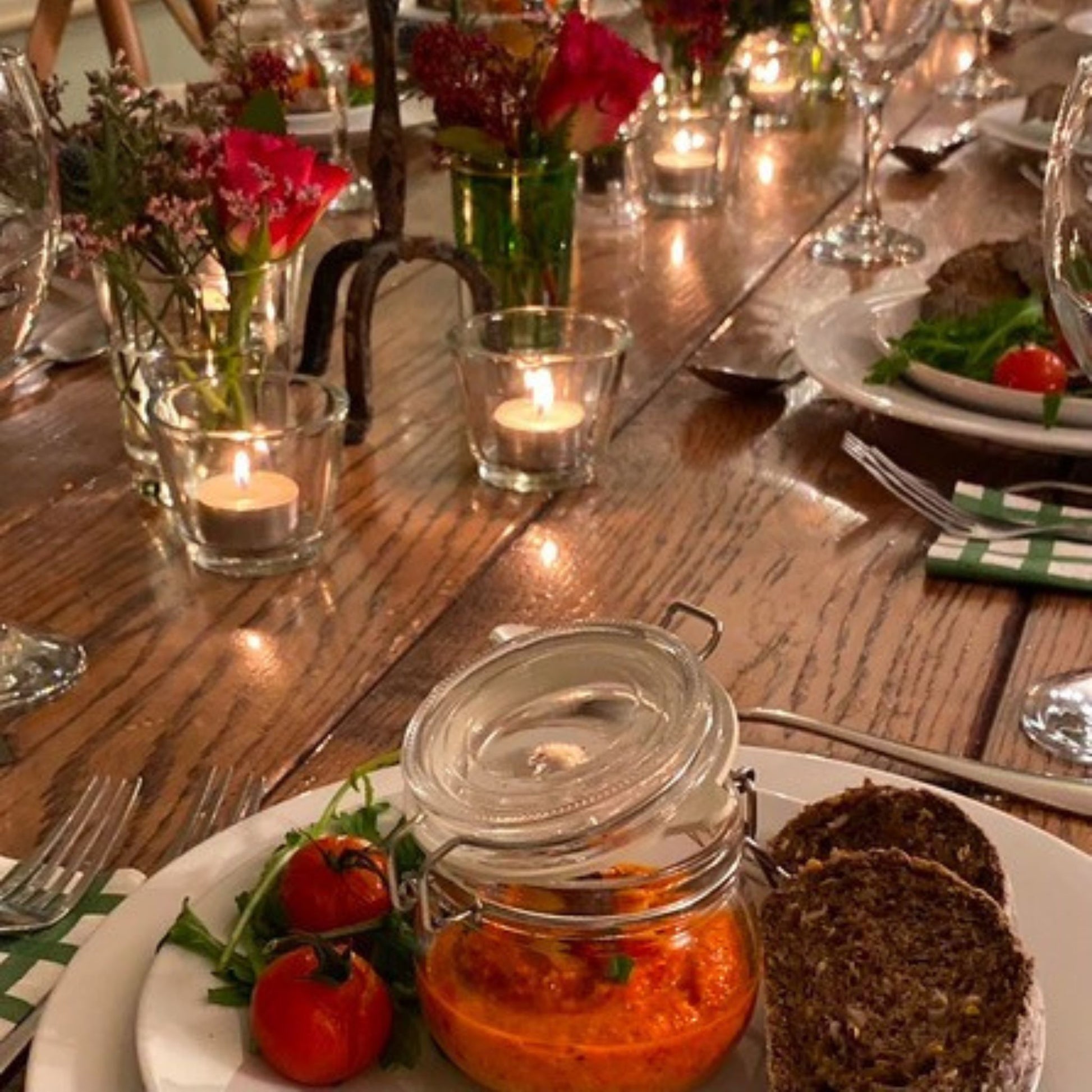 Wooden table set for dinner with tealights, andles, houmous in a jar, tomatoes, bread