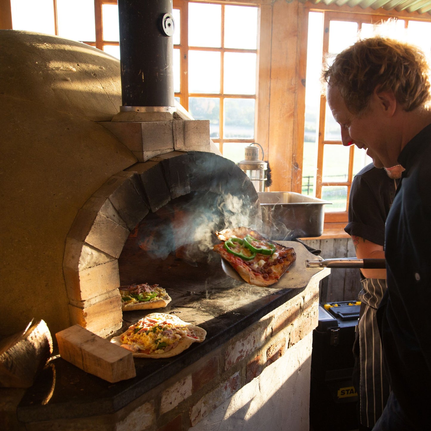Chef in front of clay oven with pizza paddle and freshly baked pizza