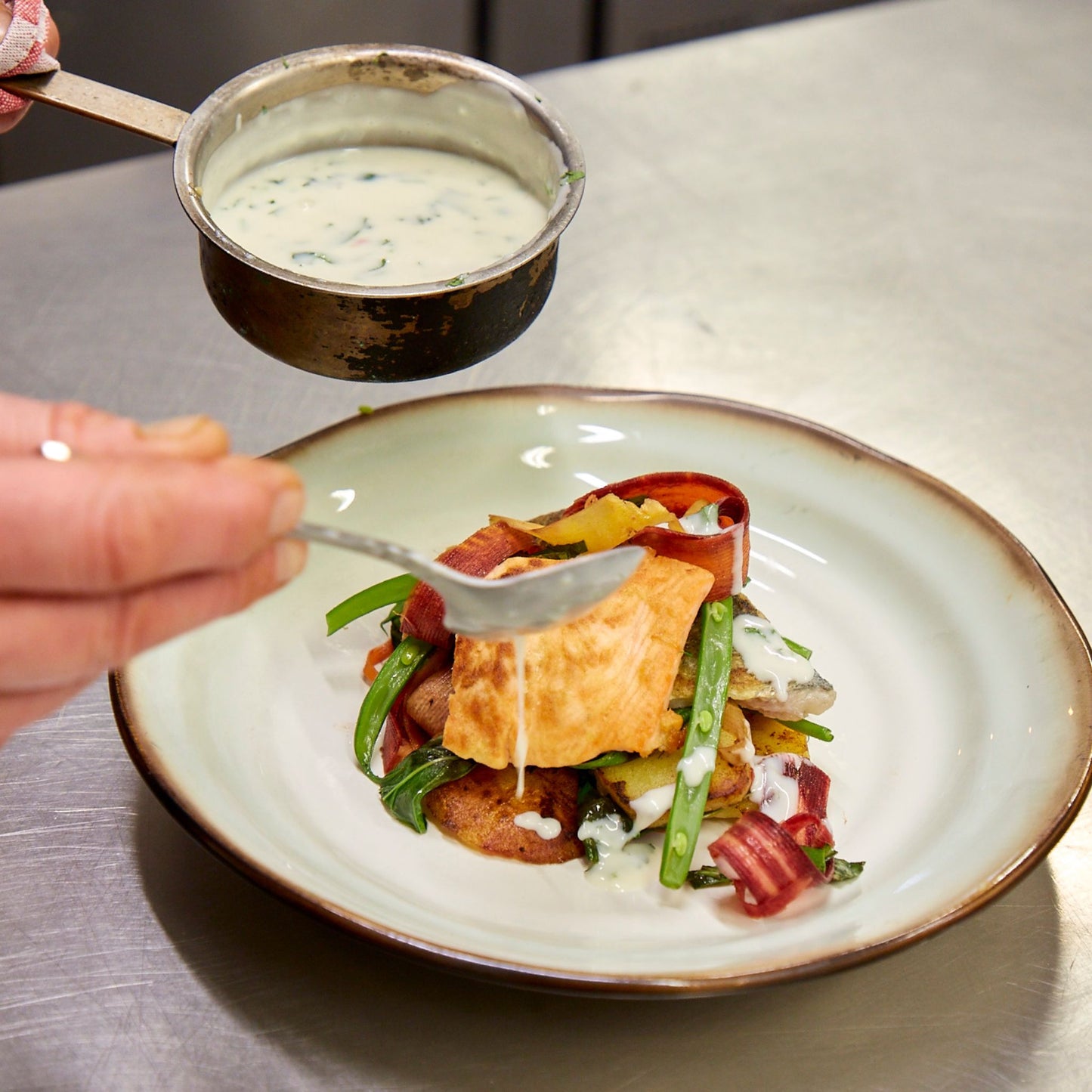 Beautifully presented fish dish with sauce being poured over