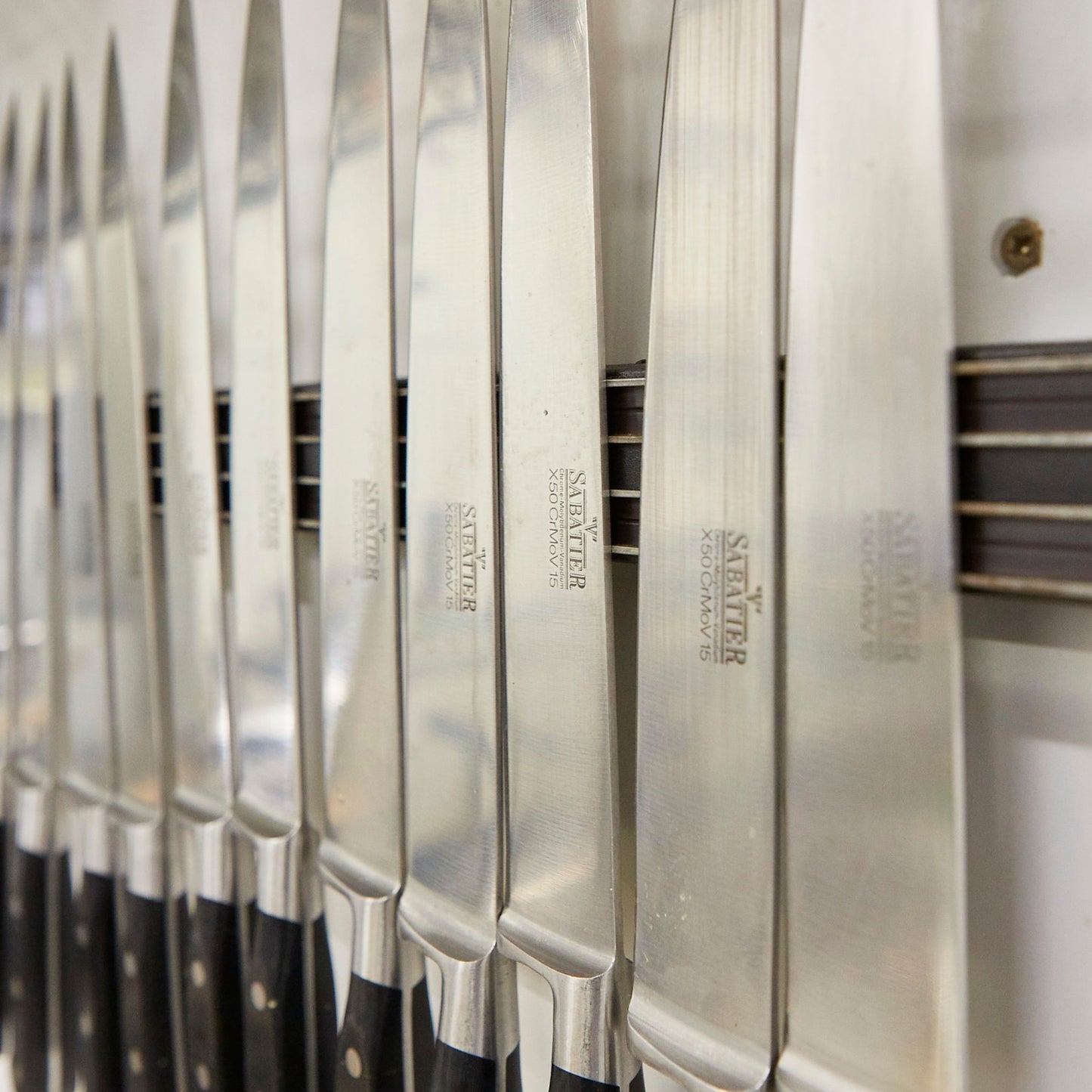 Sharp professional cook's knives hanging on a magnetic holder.