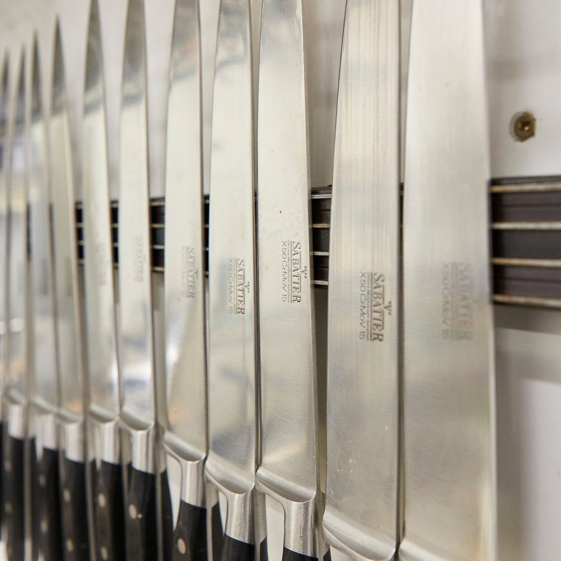Sharp professional cook's knives hanging on a magnetic holder.