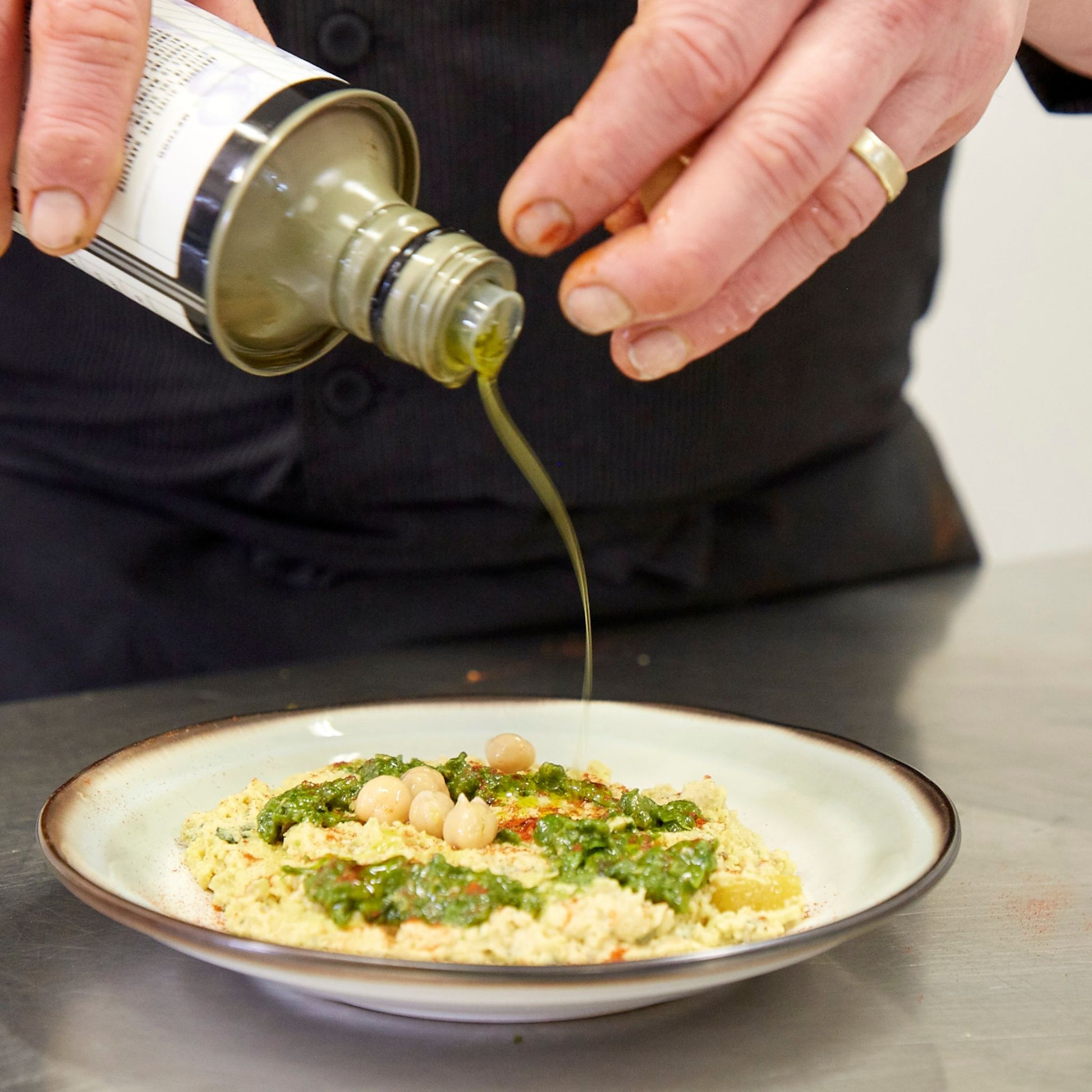 Chef drizzling oil from a bottle onto houmous plate