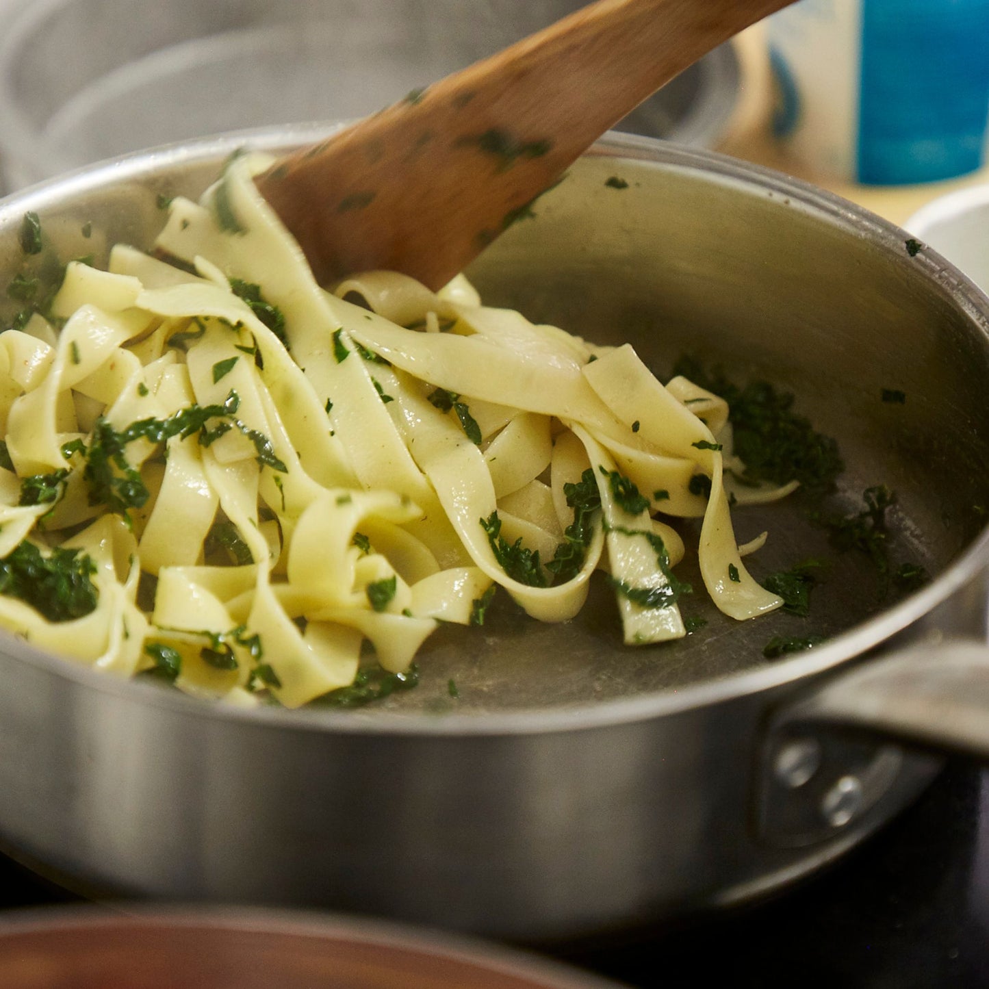 Homemade pasta being stirred with a wooden spoon in a pan.