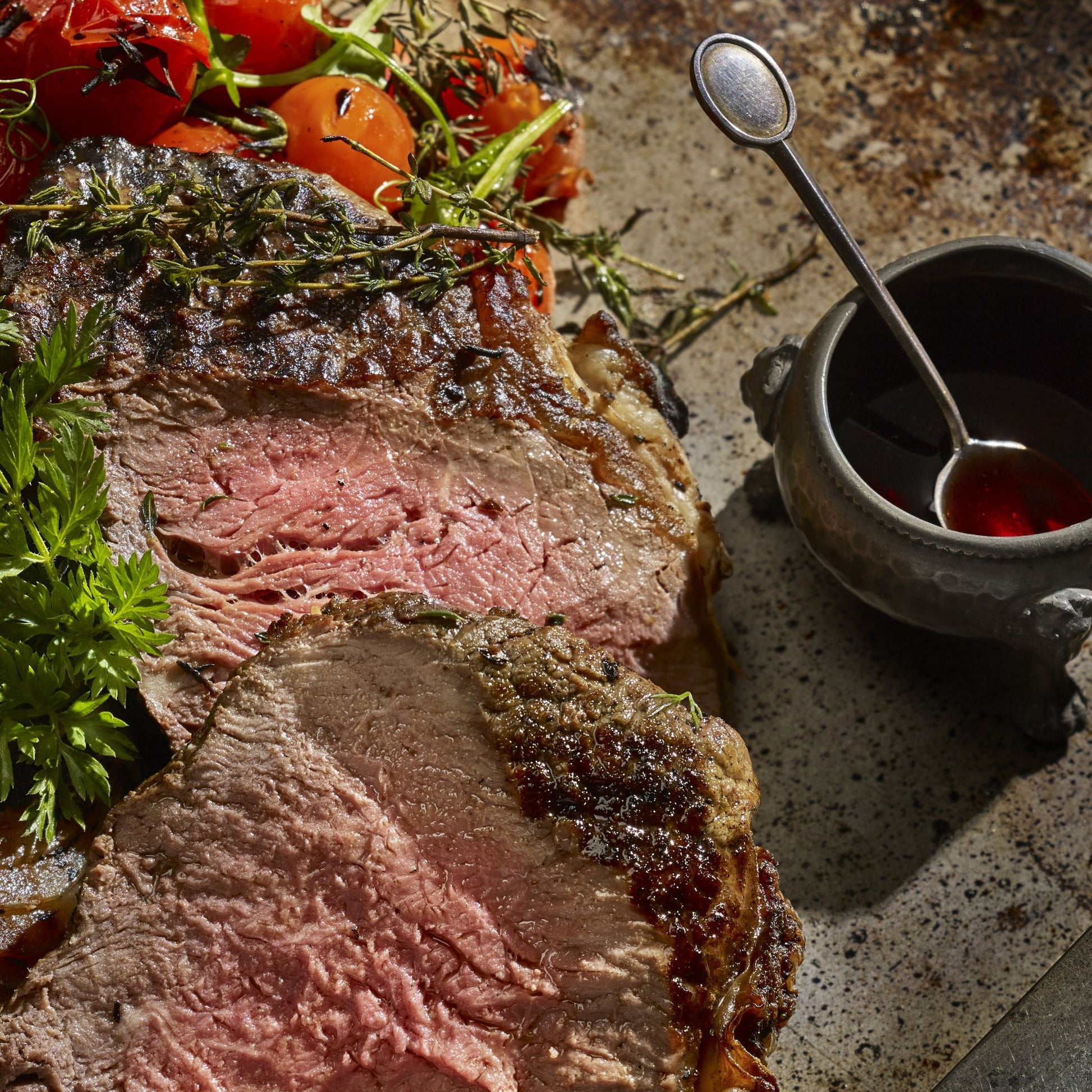 Sliced steak on a platter with a little pot of sauce