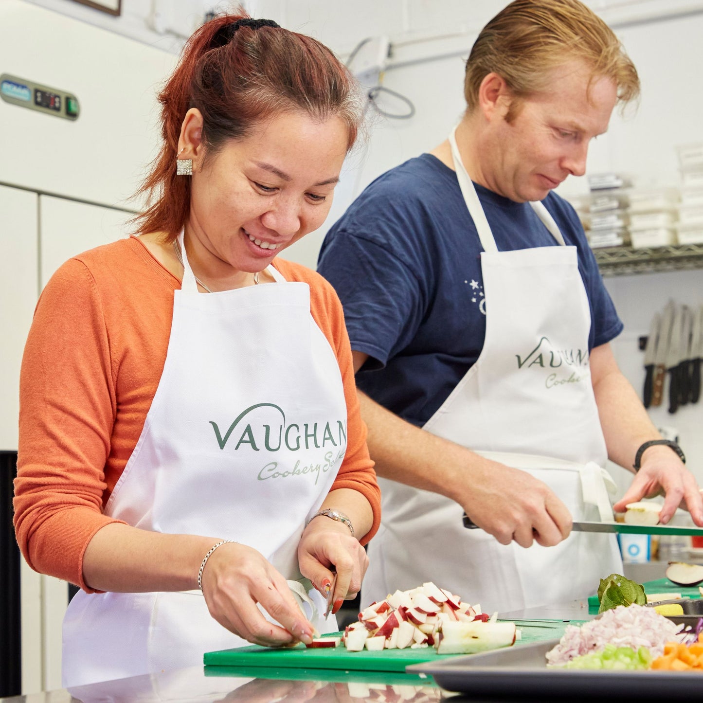 A man and a woman cooking together, wearing cookery school aprons