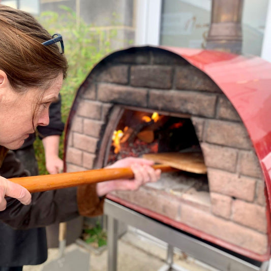 A lady with a paddle putting a dish into wood fired oven