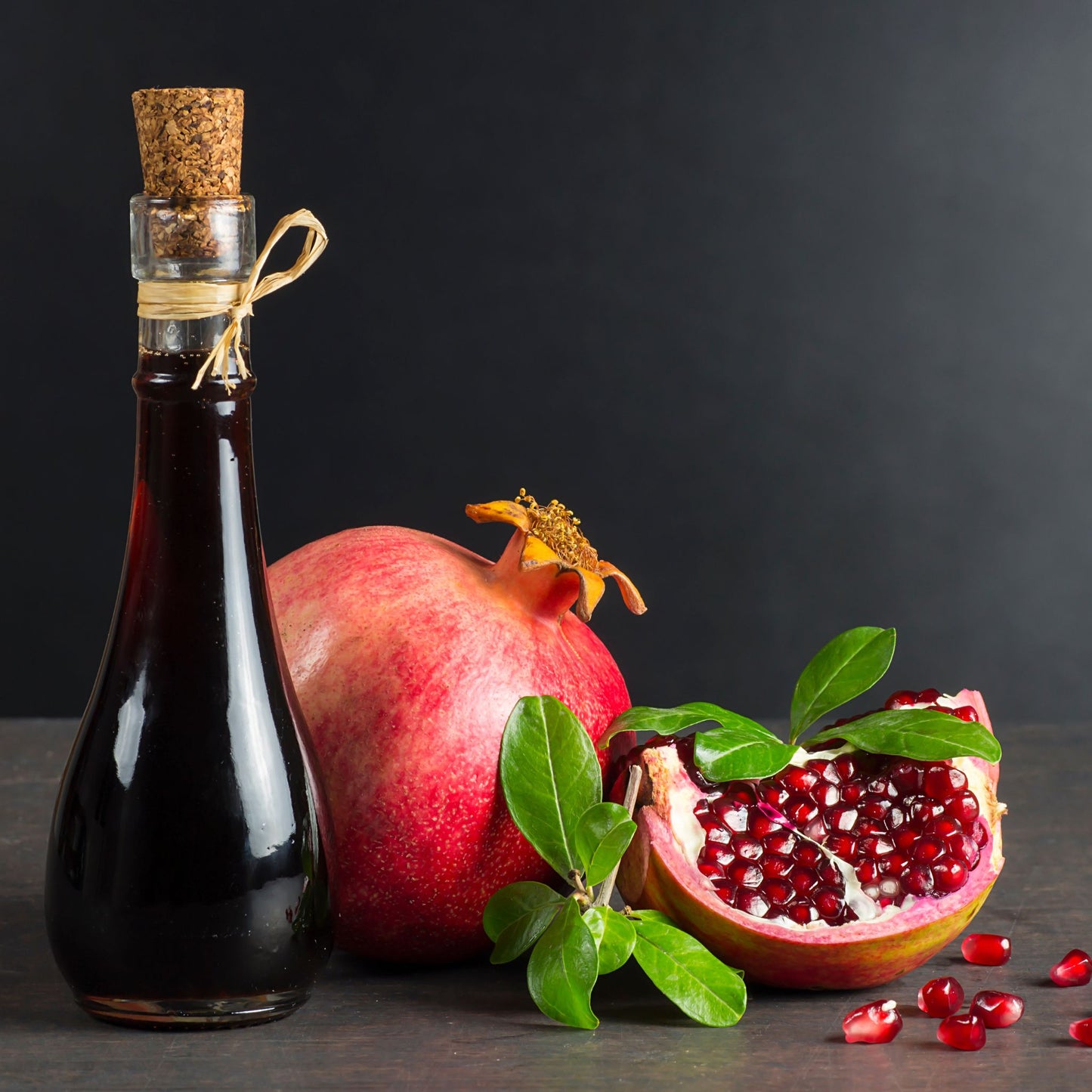 Bottle of syrup next to pomegranate on dark background
