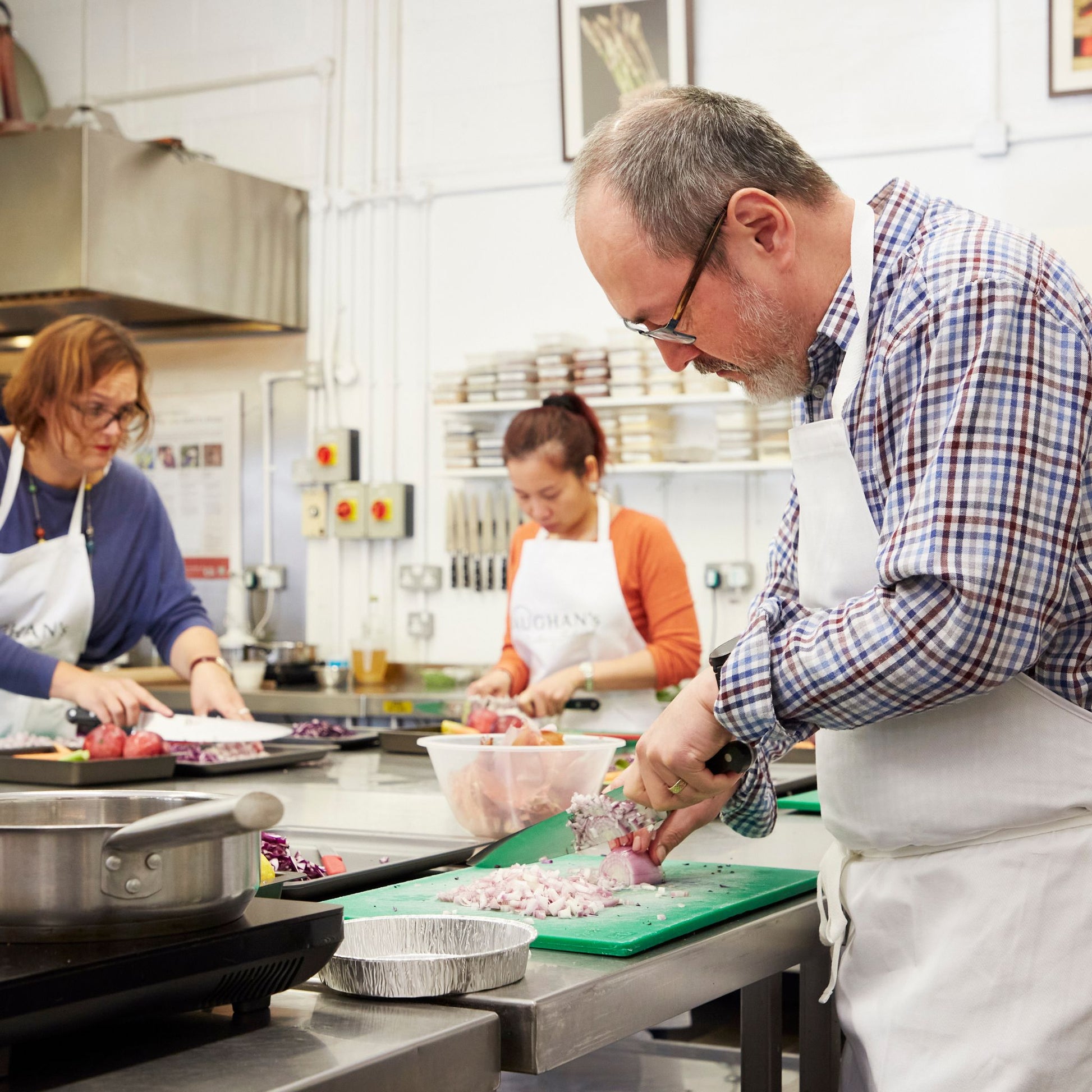 A middle aged man and two women cooking together in a kitchen