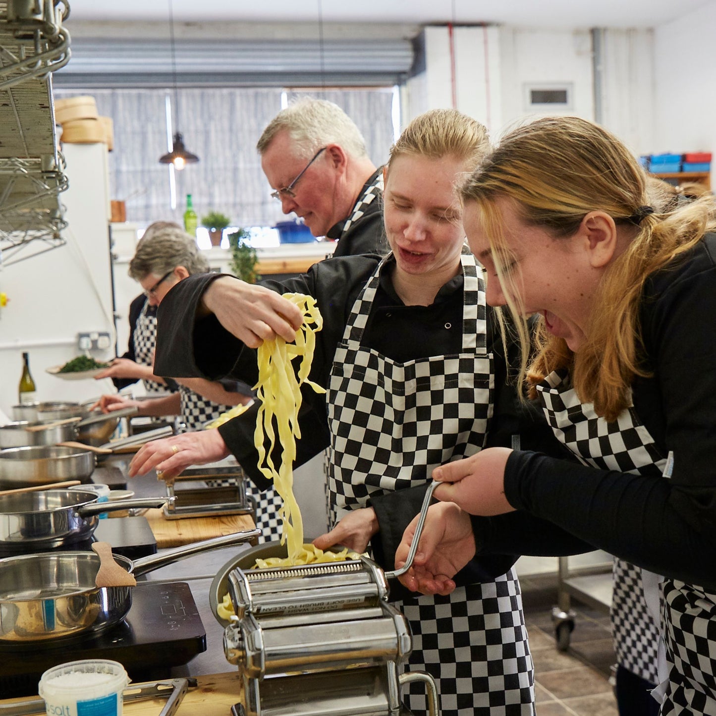 Focus on two young girls in a mixed age group of people cooking pasta together 