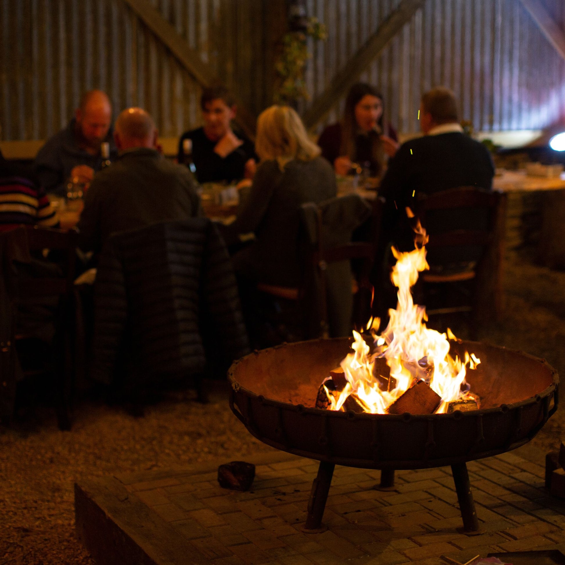 Giant fire pit, people eating at long tables, communal seating