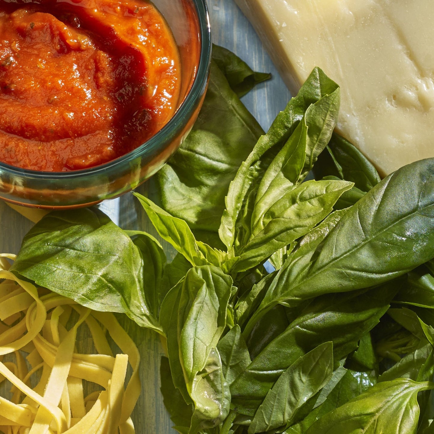 Pasta, basil, tomato sauce in a pot, block of cheese