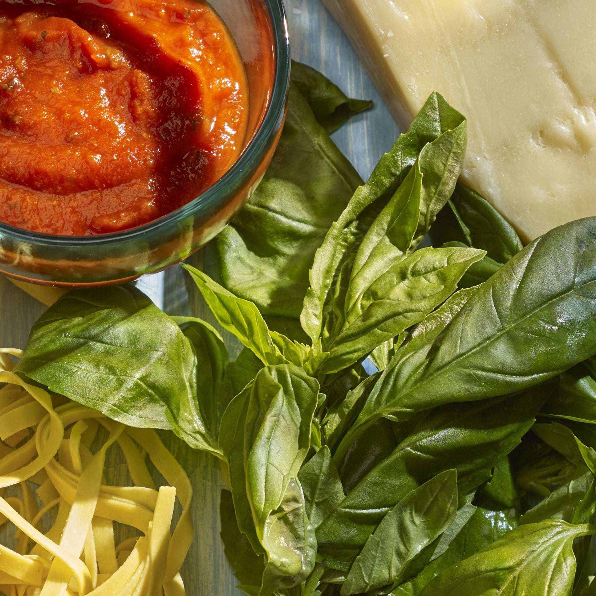 Pasta, basil, tomato sauce in a pot, block of cheese