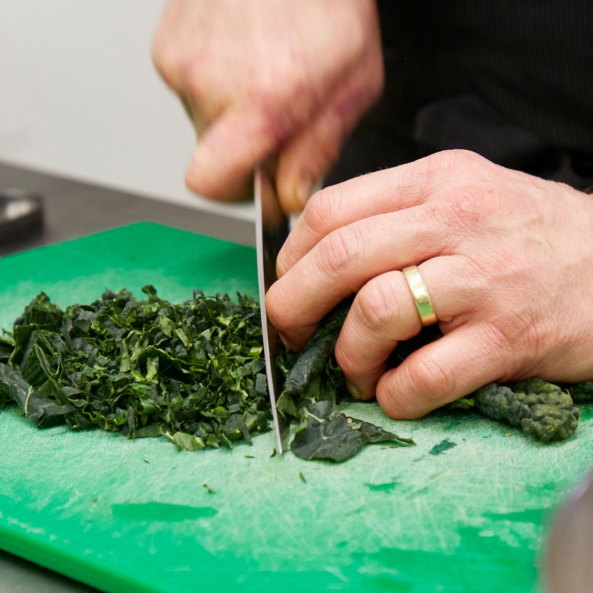 Man's hands in a bridge hold chopping cavolo nero leaves with a sharp knife