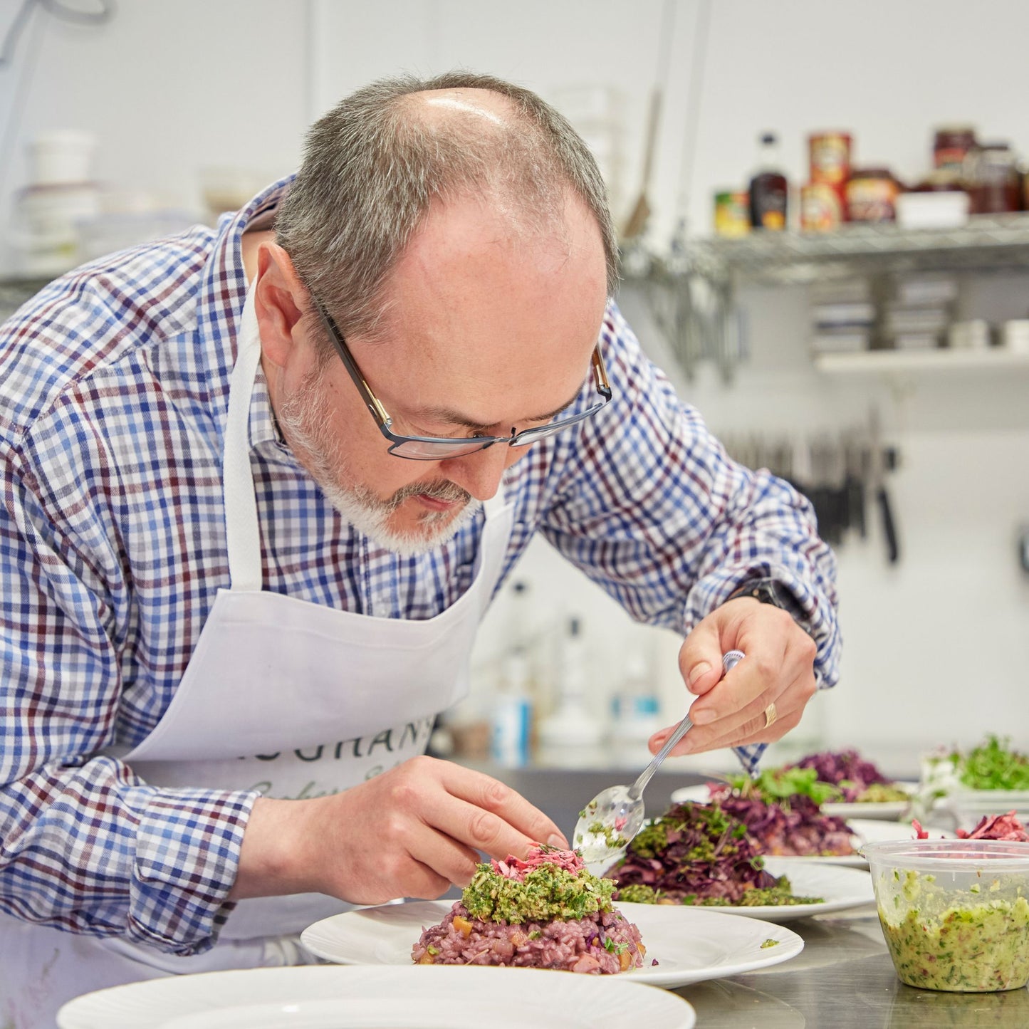 Middle aged man wearing an apron and plating a dish