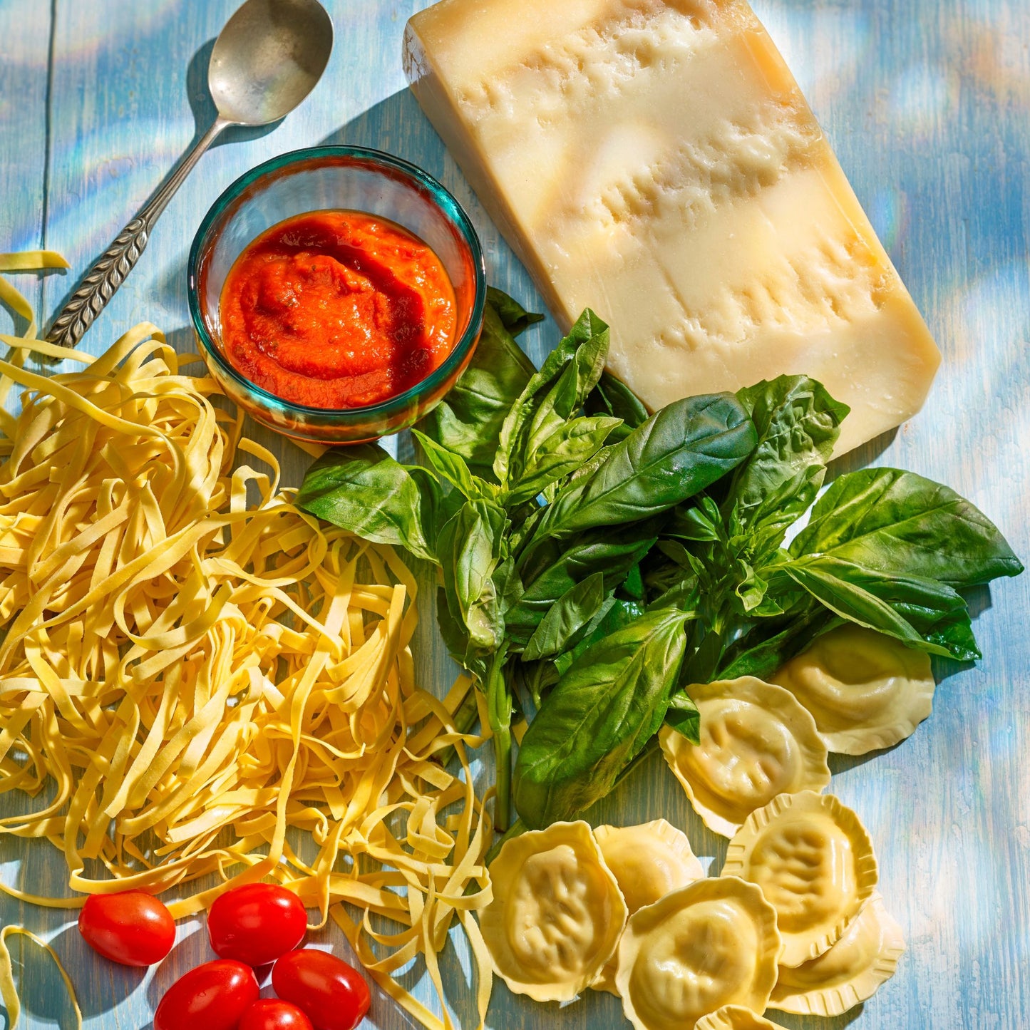 Different types of pasta laid out on a board with fresh basil, tomato sauce and cheese.