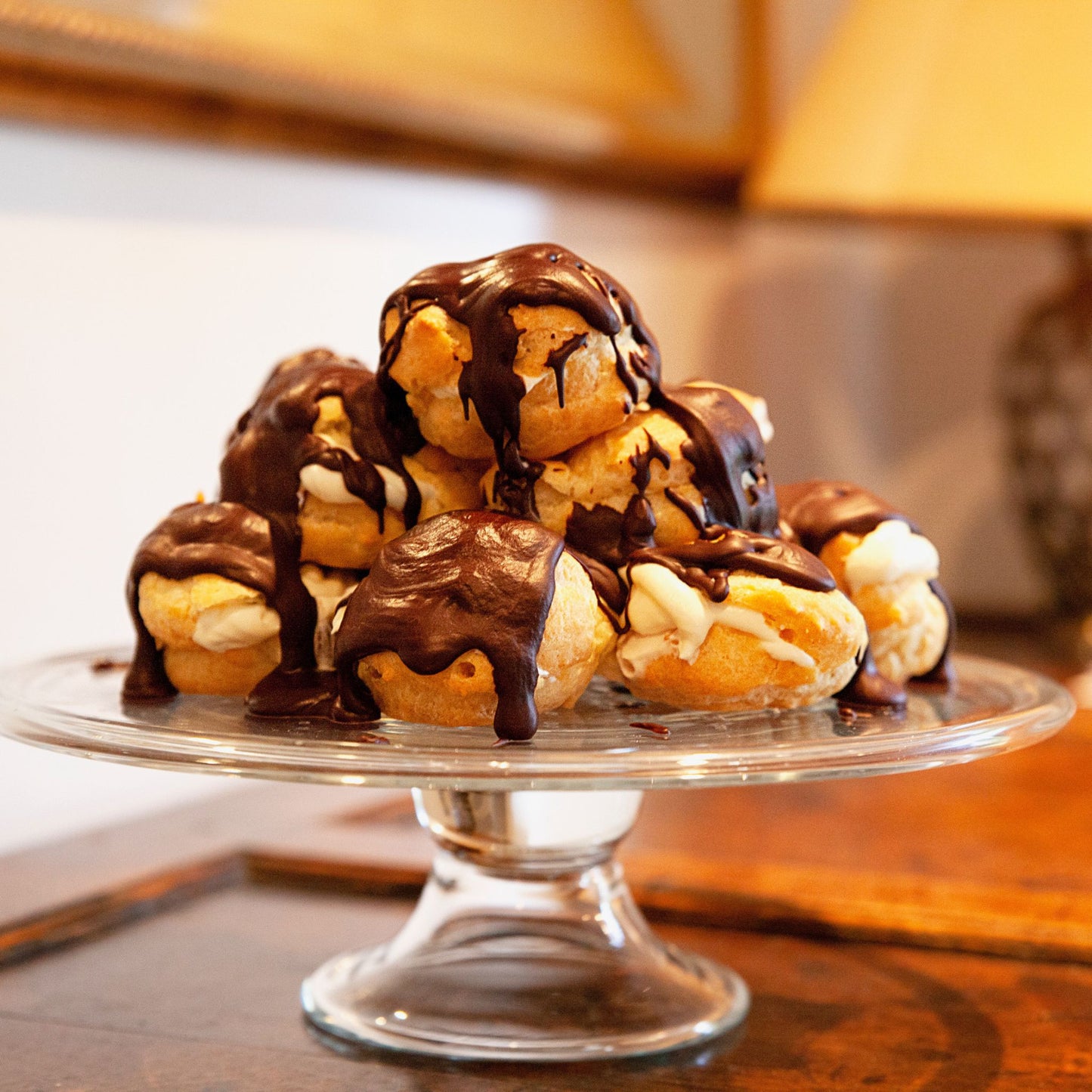 Profiteroles in a tower on a glass cake stand made with Choux pastry, cream and chocolate sauce