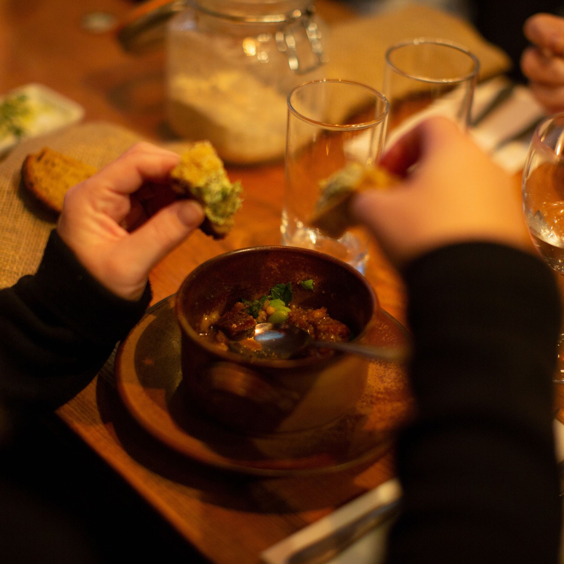 Hands dipping bread into a broth in a brown clay bowl 