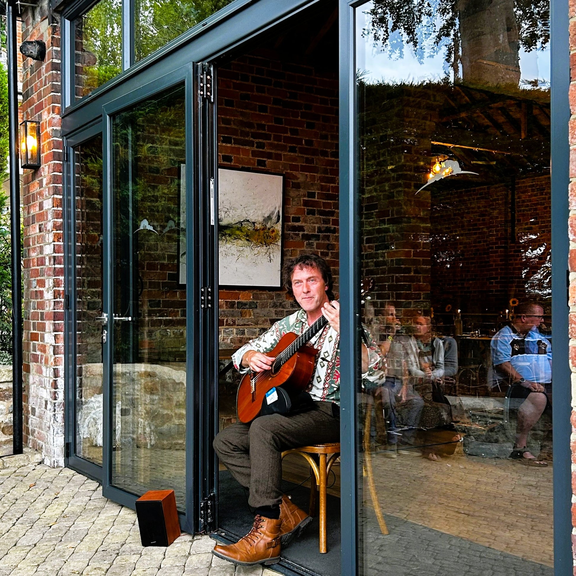Man playing a guitar sitting in the glass doorway