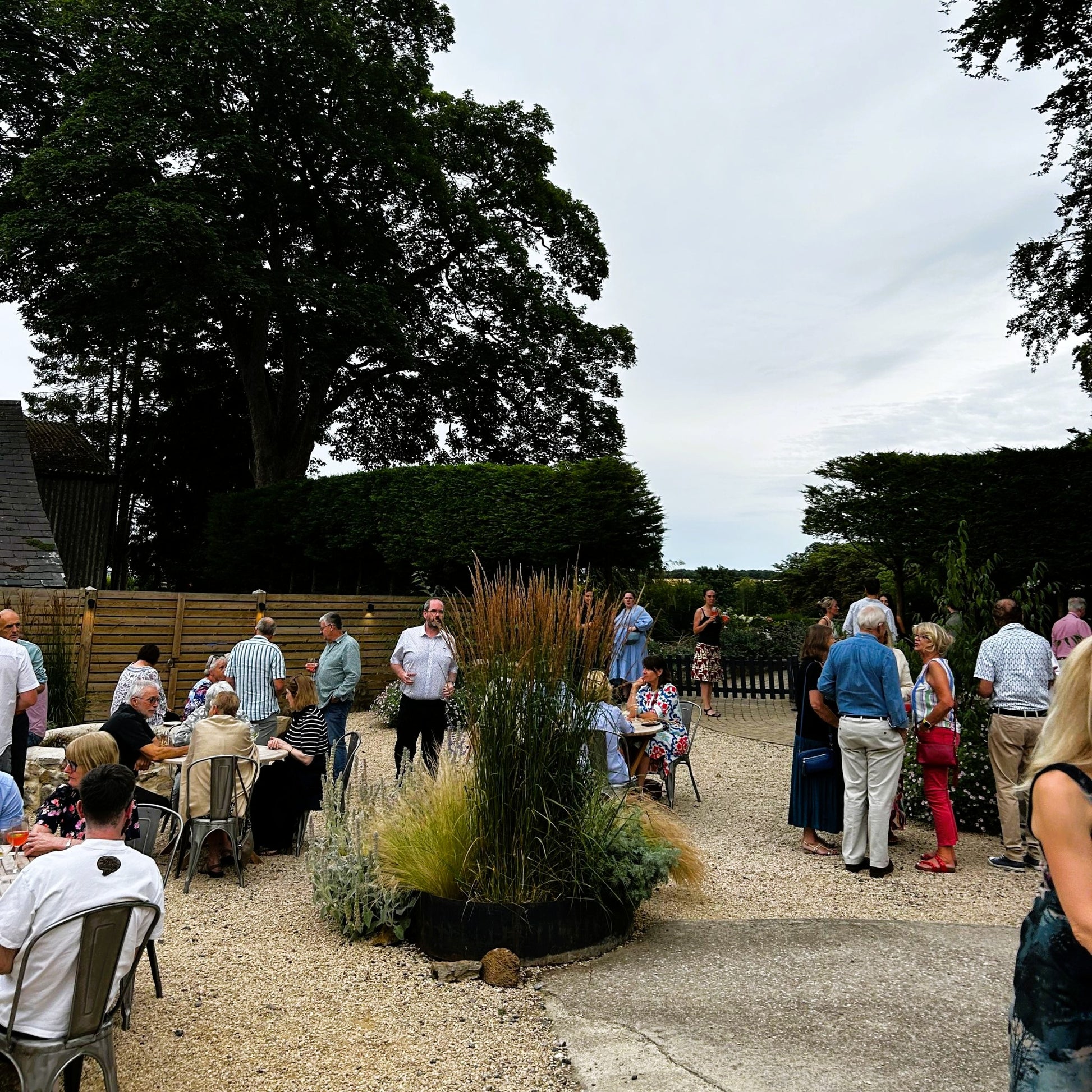 People standing and sitting at some tables in a courtyard with grasses in the middle
