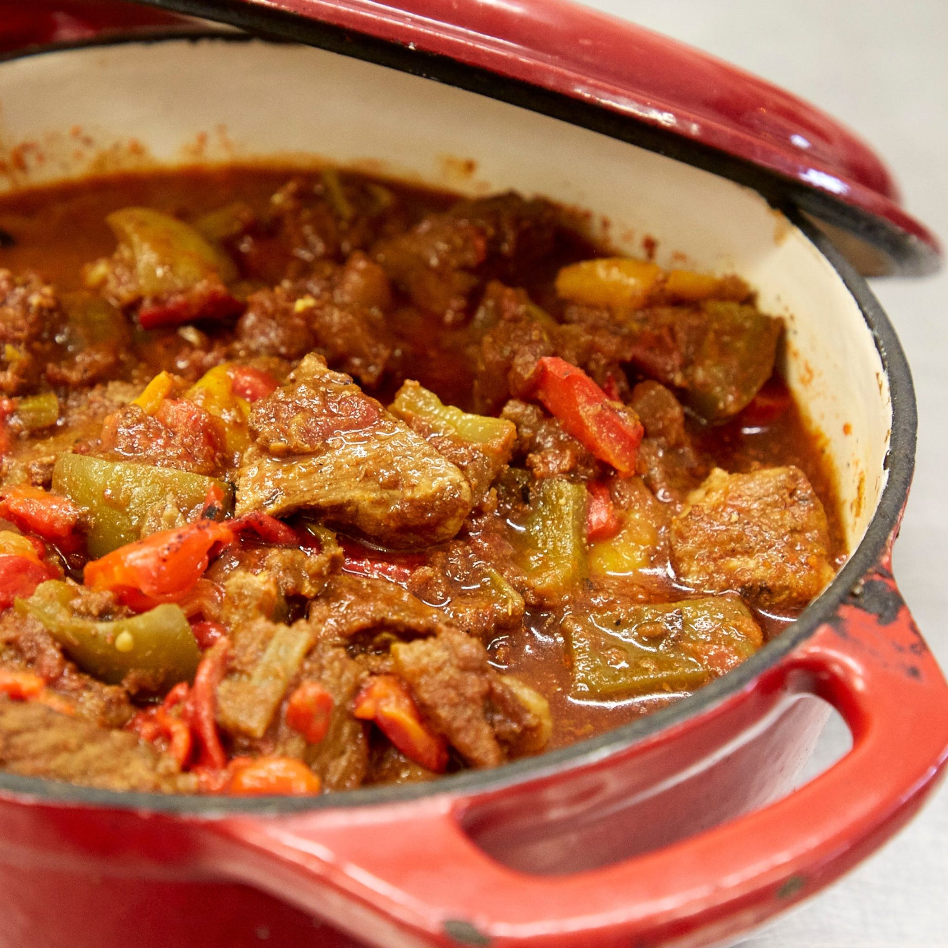 Stew of meat with red, yellow and green peppers in a red pot with handles